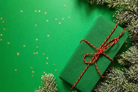 Christmas wrapped gift box and tree branches on green background with confett Foto stock