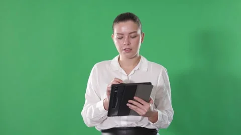Chroma key compositing. Pretty girl takes notes in electronic tablet on a green 動画素材 344844348