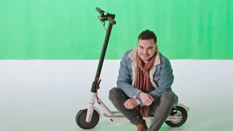 Chroma key studio sitting down man on his electric scooter looking straight to Stock Footage 135511319