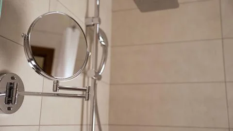 Chrome bathroom mirror with extendable arm mounted on beige tiled wall next.. 스톡 사진