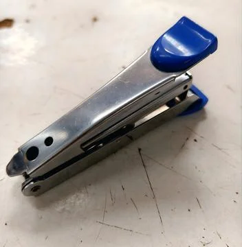 Chrome metallic office stapler resting on white work desk surface close up Stock Photos
