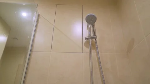 Chrome shower head spraying water against beige marble tile wall Stock Footage 343105134
