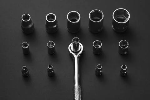 A chrome socket wrench and adapters are arranged on a dark gray surface Stock Photos