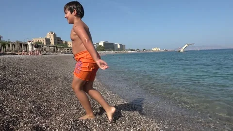 Chubby boy walking out of the sea and falling on the beach 스톡 동영상 342503326