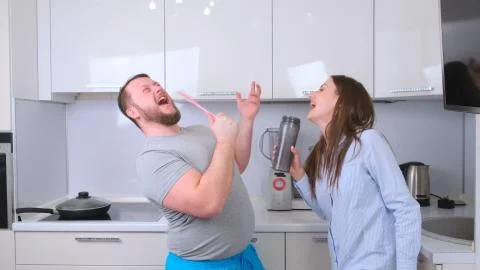 Chubby man and woman dancing and singing in the kitchen while cooking at home Stock Photos