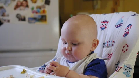 Chubby nine-month-old child sits in a child's chair and eats cookies. Stock Footage 129691302