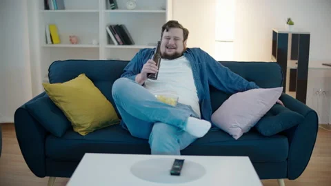 Chubby young man enjoying comedy on tv, eating chips, drinking beer at home Video stock 150633559