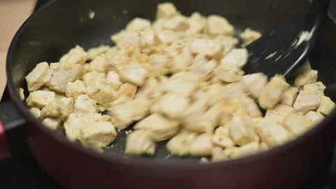 Chunks of chicken are being cooked in a skillet with regular stirring to ensure 库存影片 338298530