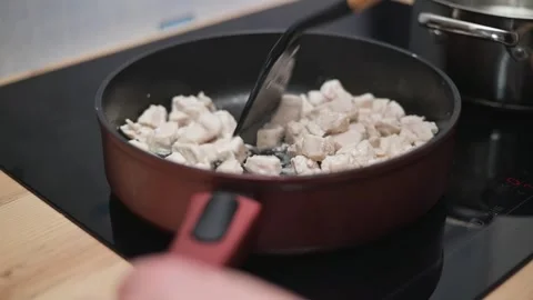 Chunks of chicken are being stirred in a pan on a stovetop in a home kitchen. Stock Footage 338298409