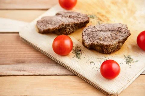 Chunks of deep-fried meat, steak on a wooden tray with spices and cherry toma Stock Photos