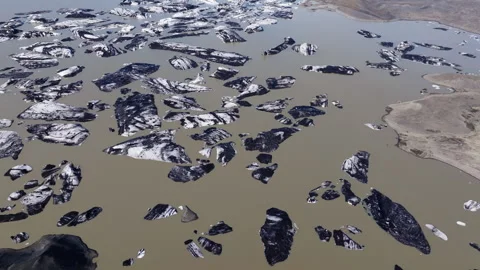 Chunks of ice in murky brown glacier lagoon with volcanic ash and debris Stock Footage 340192559
