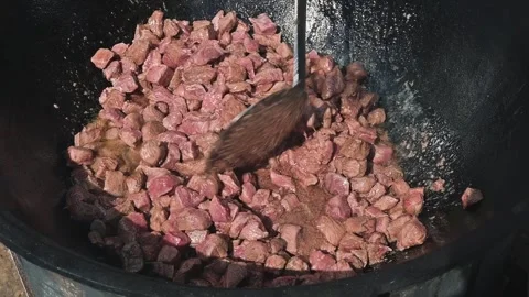 Chunks of meat are being cooked in a large pot over a heat source. Stock Footage 345882461