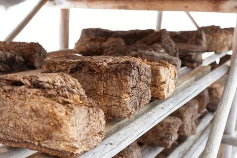 Chunks of peat piled up for drying on wooden shelf . Horizontal photo with bl Stock Photos