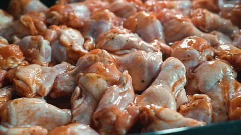 Chunks of raw chicken wings are coated in rich sauce, preparing for cooking. Stock Footage 338290340