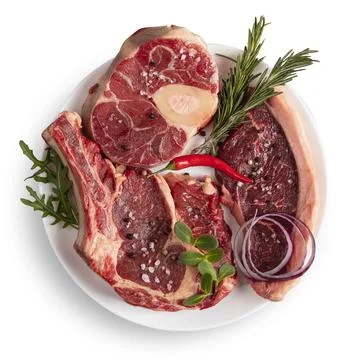 Chunks of raw meat on a white plate. Chili pepper, rosemary, onion, spices. I Stock Photos