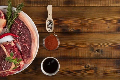 Chunks of raw meat on a white plate. Chili pepper, rosemary,  spices. Wooden  Stock Photos