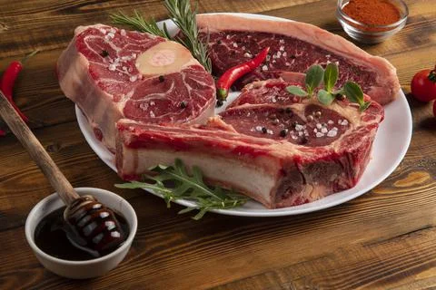 Chunks of raw meat on a white plate. Chili pepper, rosemary, onion, spices. W Stock Photos