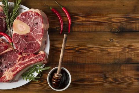 Chunks of raw meat on a white plate. Chili pepper, rosemary, spices. Wooden t Stock Photos