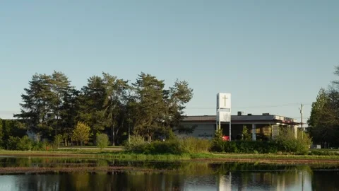 Church building with cross surrounded by trees and pond in a serene park Stock Footage 276341849