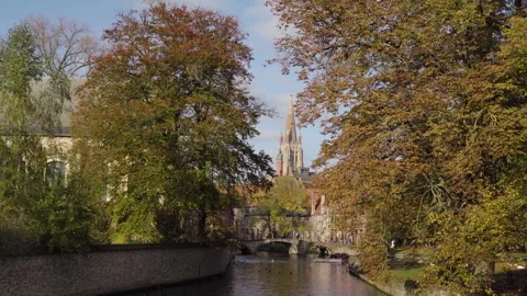 Church of Our Lady tower with river between trees on sunny fall day in Bruge Stock Footage 329052710