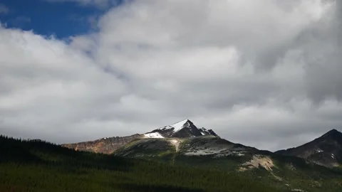 Churning white and gray clouds above triangular shaped snow-covered mountains  Stock Footage 141156048