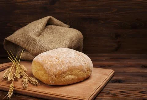 Ciabatta bread with ears of wheat and burlap over dark wooden table backgroun Stock Photos