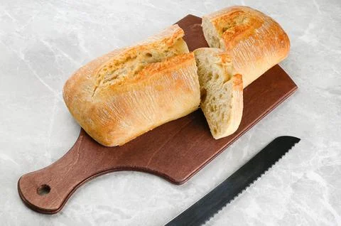 Ciabatta rustic bread beautifully cut on a cutting board with a bread knife. Stock Photos