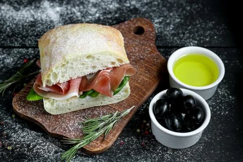 Ciabatta sandwich with arugula salad, spinach leaves, bacon on a wooden board Fotos de archivo