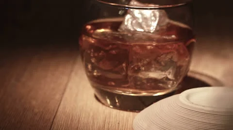 Cigar being placed beside tumbler of whiskey on the rocks Stock Footage
