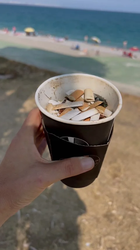 Cigarette buds in a cup at the beach hand held Vidéo 230450786