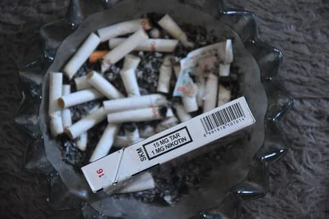 Cigarette butts in an ashtray full of ashes, placed on the carpet, plus a t.. Stock Photos