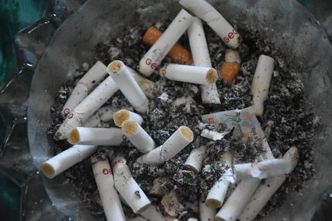 Cigarette butts in an ashtray full of ashes, placed on the carpet, plus a t.. Stock Photos
