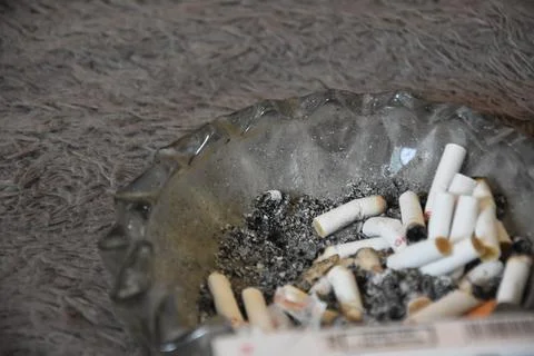 Cigarette butts in an ashtray full of ashes, placed on the carpet, plus a t.. Stock Photos