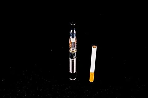 A cigarette is next to a vape Stock Photos