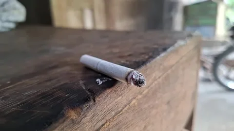 The cigarette placed on the wooden table emits white smoke Stockbeeldmateriaal 255214934