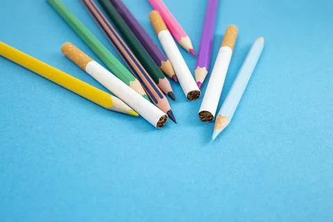 Cigarettes between colored crayons on blue paper backdrop Stock Photos