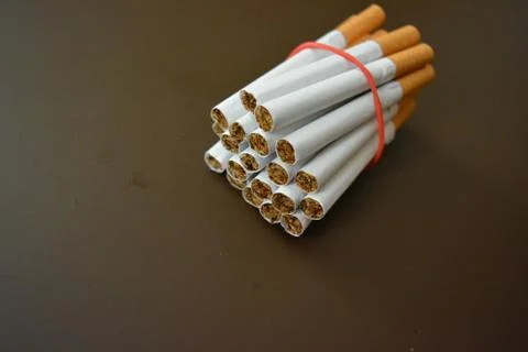 Cigarettes from the pack are fixed with a red rubber band on brown background Stock Photos