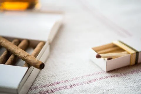 Cigars and whiskey on a light table cloth, one cigar out of the packet Stock Photos