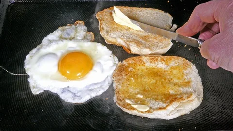 Cinemagraph – Egg frying with man’s hand holding a buttered knife over toast. 스톡 동영상 129175199
