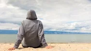 Cinemagraph - Man Or Woman Is Sitting In A Hoodie On The Beach. Back View. 4K Stock Footage