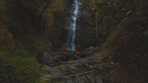 Cinemagraph of man sitting in front of beautiful waterfall hidden in forest Stock Footage 87306224