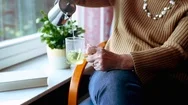 Cinemagraph Of Older Woman Pouring Tea In A Glass And Sitting By The Window Stock Footage