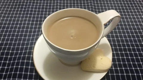 Cinemagraph - Steaming white cup of coffee with heart shaped cookie on a table Stock Footage 100789128