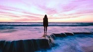 Cinemagraph Of Woman Standing On Sea Rocks With Pink Sky. Zoom In Stock Footage