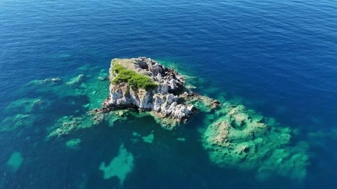 Cinematic 4K drone orbit shot around isolated rocky islet in deep blue and turqu Stock Footage 340569864