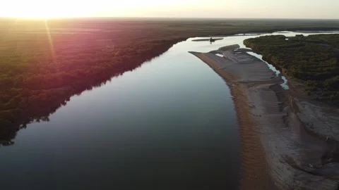 Cinematic aerial view of sun rays shining over river and forest at sunset Видео 334624849