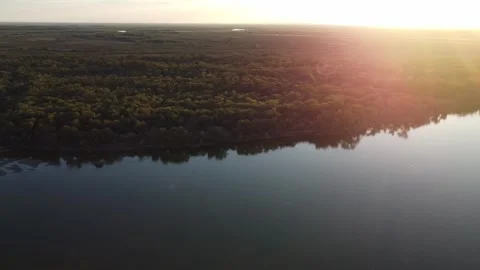 Cinematic aerial view of sun rays shining over river and forest at sunset Stock Footage 335079338