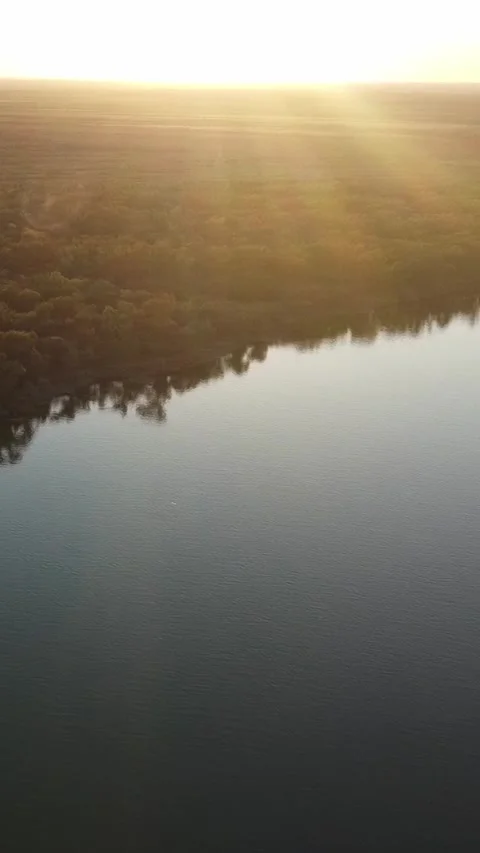 Cinematic aerial view of sun rays shining over river and forest at sunset Stock Footage 336686761