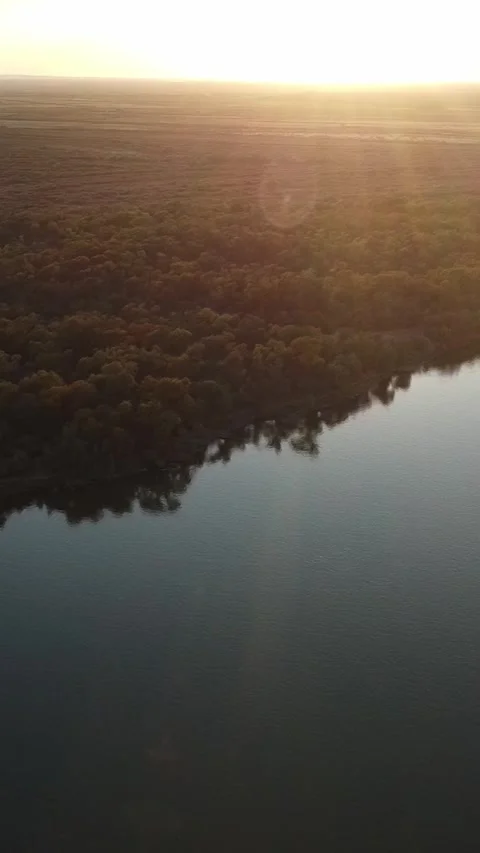 Cinematic aerial view of sun rays shining over river and forest at sunset Stock Footage 336686823