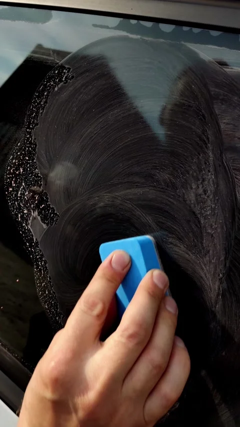 Cinematic close-up of a hand scrubbing car window with foam Stock Footage 334129169